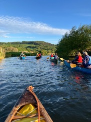 People in canoes on water, with countryside in the background