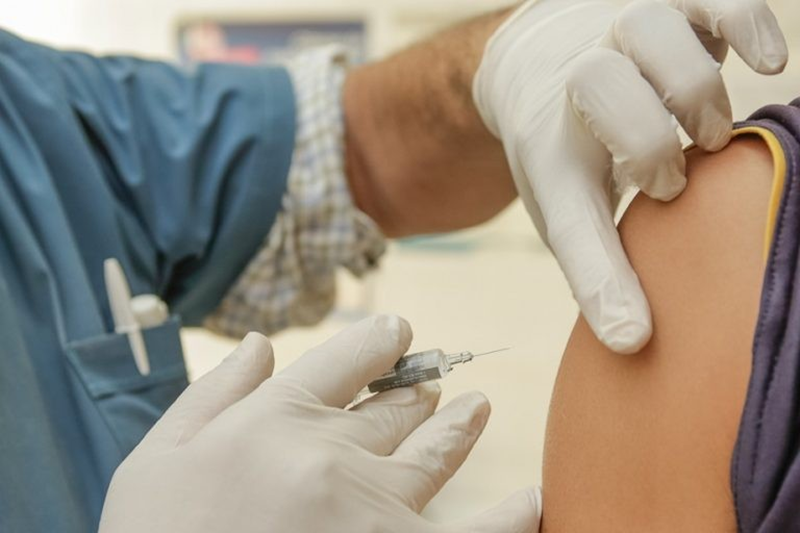 An injection being given in the top of a persons arm by a medical professional