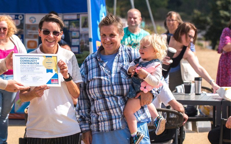 Two tenants, one holding a toddler, receiving the certificate for "Outstanding Community Contributor"