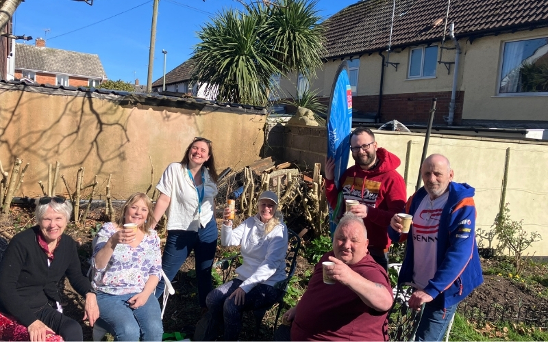 Tenants of Tully Gardens and Jamie Clayden Communities Officer all smiling and raising their hot drinks outside in the community garden