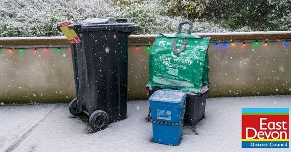 East Devon recycling containers with Christmas hanger. Snow falls and Christmas lights hang from a wall