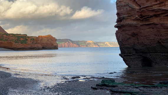 By the water's edge with brown cliffs to the right and in the background 
