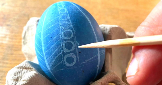 A person etching a design into a blue egg