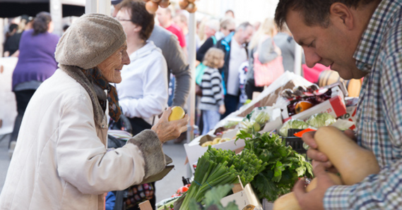 Crowds of people at a market, with a fresh produce stall in the foreground