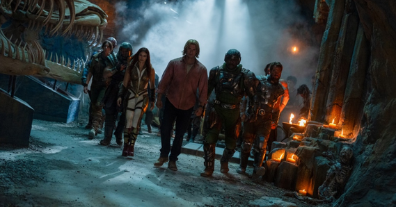 Group of actors in costume walking through a cave lit with candles, with a large skull