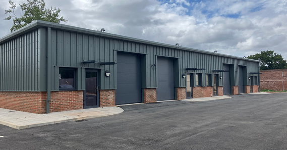 A clad business space with windows, doors, and garage doors, with tarmac in front
