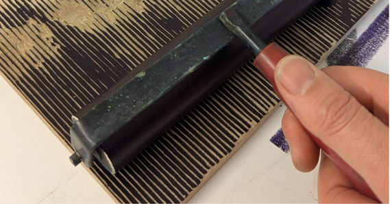 A hand holding a tool, as part of a printmaking process