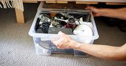 Plastic box of small electrical items being pulled out from beneath a bed