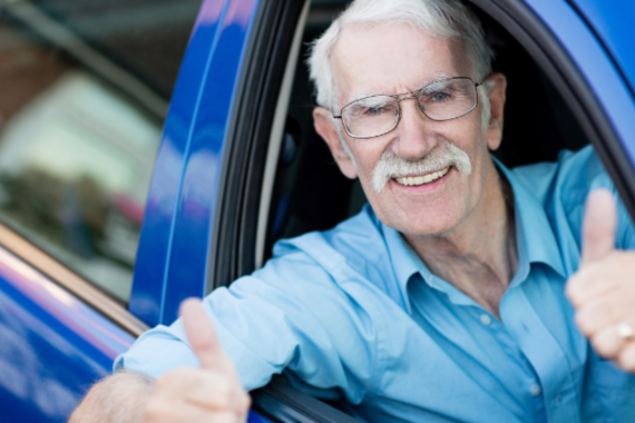 Man holding his thumbs up and sitting inside a blue car.