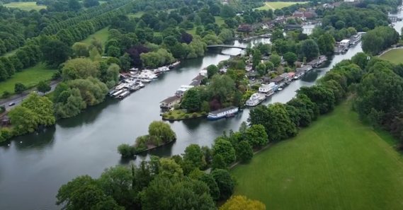 Drone image of river with green space and houses along the river.