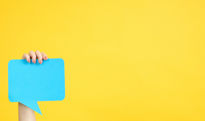 A hand holding up a speech bubble prop