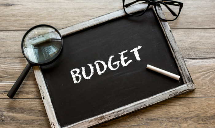 Budget written on a small hand held blackboard with a magnifying glass and glasses next to it