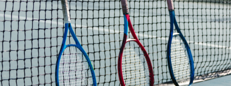 Three tennis rackets leaning against a net