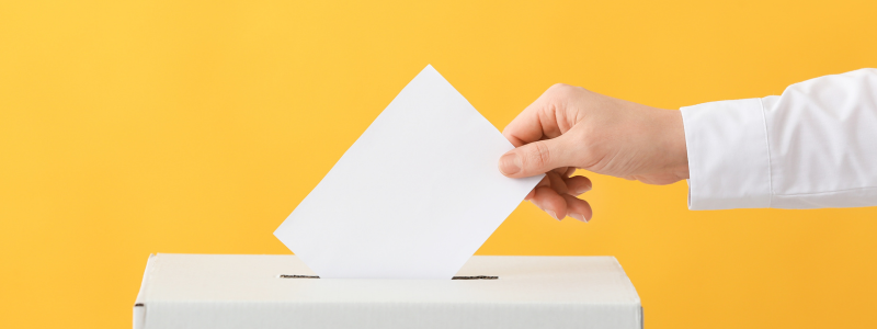 Hand putting ballot into a box on a yellow background