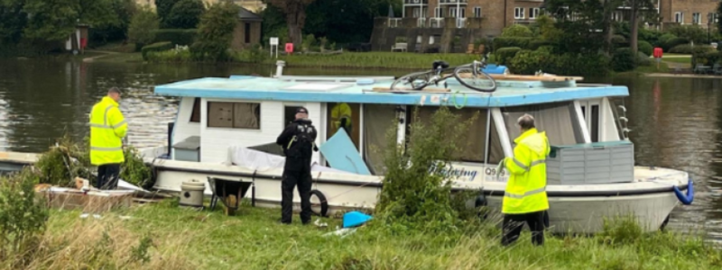 Two people in hi-vis jackets and a police officer by a boat on the river