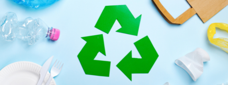 Plastic plate, fork, bag and water bottle around a green recycling sign