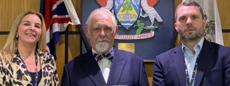 Three people standing in front of Elmbridge Council coat of arms including the Chief Executive, Adam Chalmers