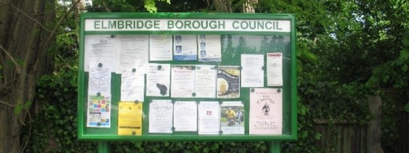 Elmbridge community noticeboard with posters on it in a green space