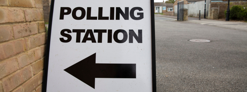 Sign with the words polling station and an arrow pointing to a brick building