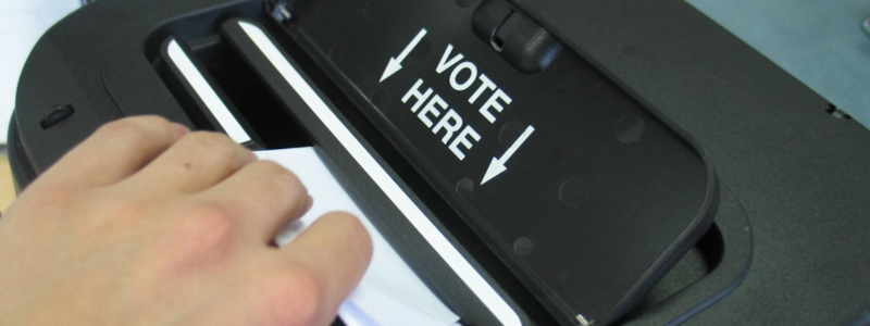 Hand casting a vote into a ballot box