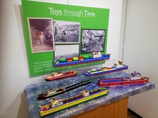 Ships made from Lego on display in a museum, with photos of toys a board behind them