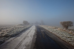 Photograph of road with two grassy verges, disappearing into fog.