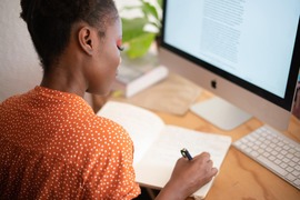 woman writing in a notebook while looking at a computer screen