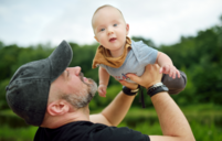 A photo of a man holding a baby in the air and smiling at them