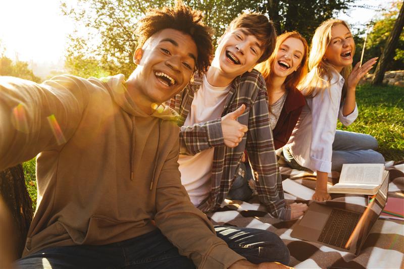four teenagers taking a selfie sitting in the park 