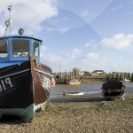 A wooden boat sitting on a pebble beach next to the waters edge