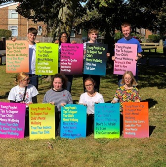 Eight members of the East Sussex Youth Cabinet hold up colourful posters printed with their ten top tips for parents for mental health and wellbeing