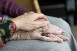 an older person has their hands on their knee and a second person lays their hand over the top to show support