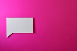 a white speech bubble cut out of paper in front of a pink background