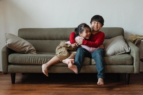 A brother and sister hugging on the couch with big smiles. 