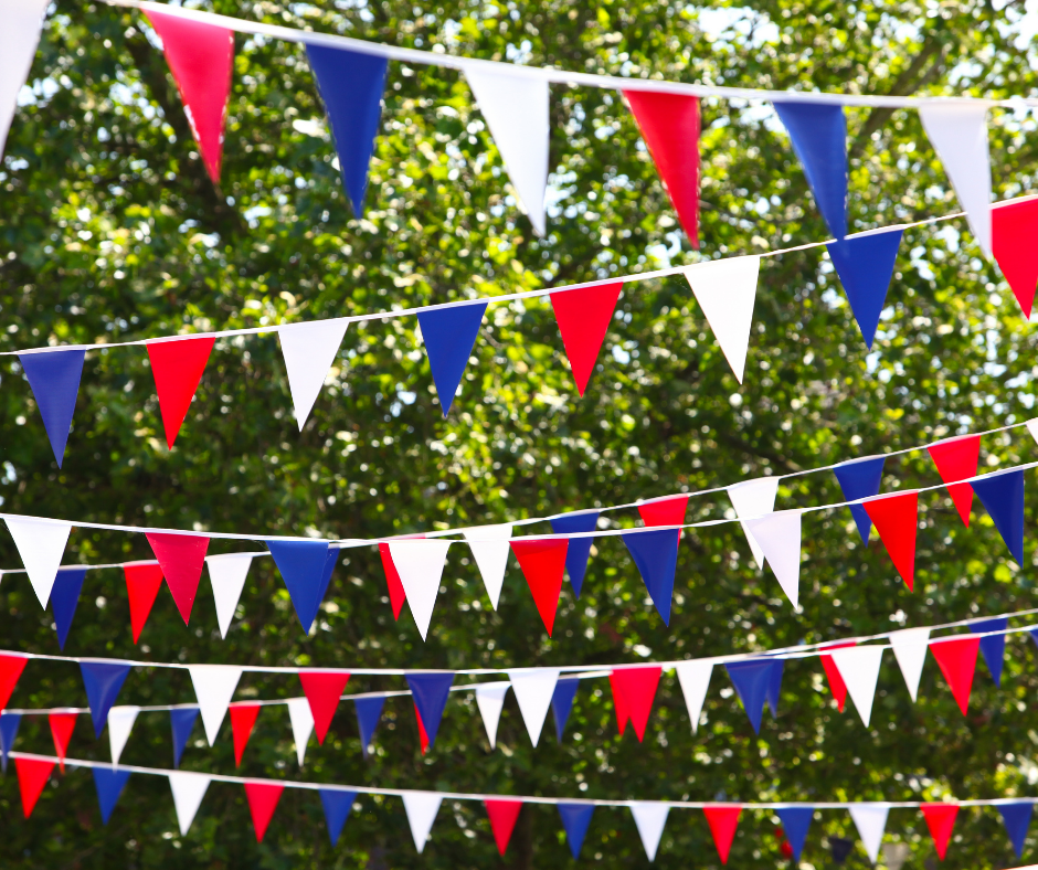 Lengths of red, white and blue bunting flutter on a sunny day with a leafy background