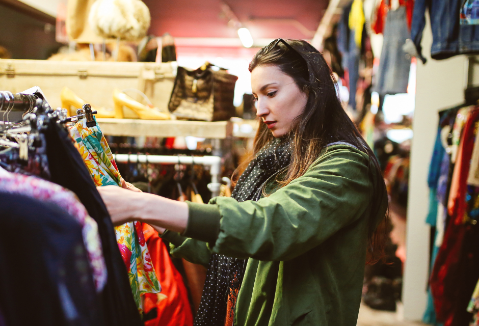 A woman rummages through clothes on a charity shop clothes rail