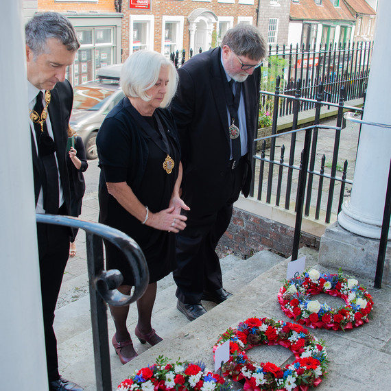 Wreaths are laid by three people with bowed heads