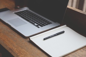 A laptop, notepad and pen on a desk