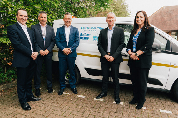 Four people wearing business suits standing in front of a van with the logos for East Sussex Highways, ESCC & Balfour Beatty