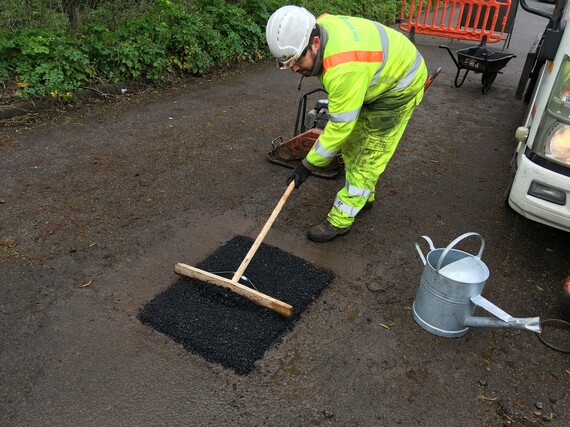 a man in high vis protective clothing filling a pothole