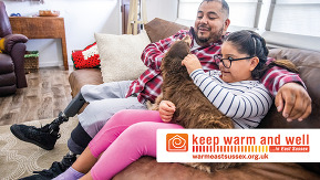 man and girl sitting on couch with a dog. Logo states 'keep warm and well in east ussex'