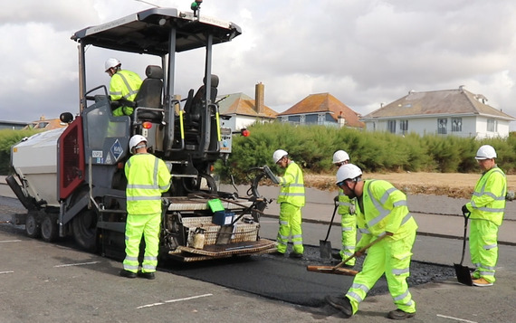 People in high-vis clothing patching a section of road, with machinery behind them