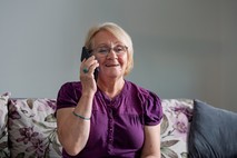 Smiling senior woman using phone whilst sitting on a sofa at home