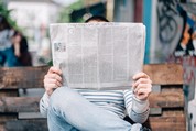 Person sitting on a bench outside reading a newspaper