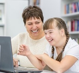 Teacher smiles at young girl using a laptop