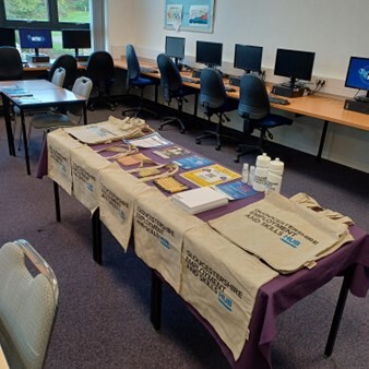 Some tables set up with leaflets and merchandise such as tote bags and water bottles on them.