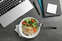 A chicken salad next to a laptop and notebook.