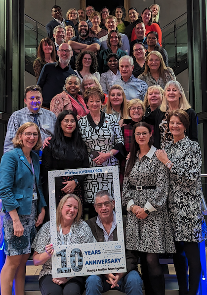 Lots of people stood on stairs with a selfie-frame at the front saying 10 years of the Strategic Clinical Networks