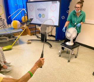 Photo of a nurse playing an air hockey game with patients.