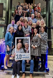 Photo of the Strategic Clinical Network team stood on a flight of stairs with a sign being held saying 10th anniversary.